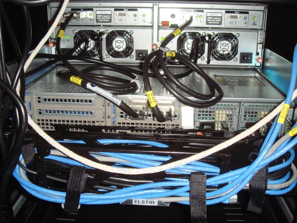 Parte trasera de una cabina de discos con ventiladores, cables azules y negros y etiquetas ELSTIR.