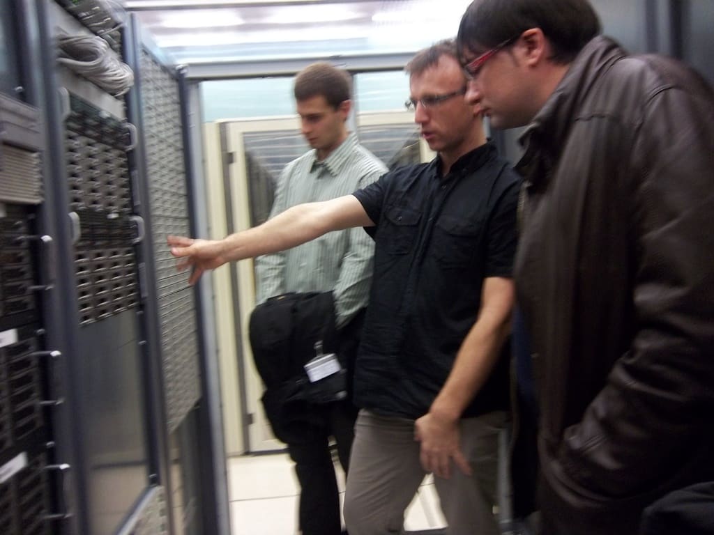 Tres técnicos ante un rack de red abierto en un CPD; uno señala los módulos del equipo