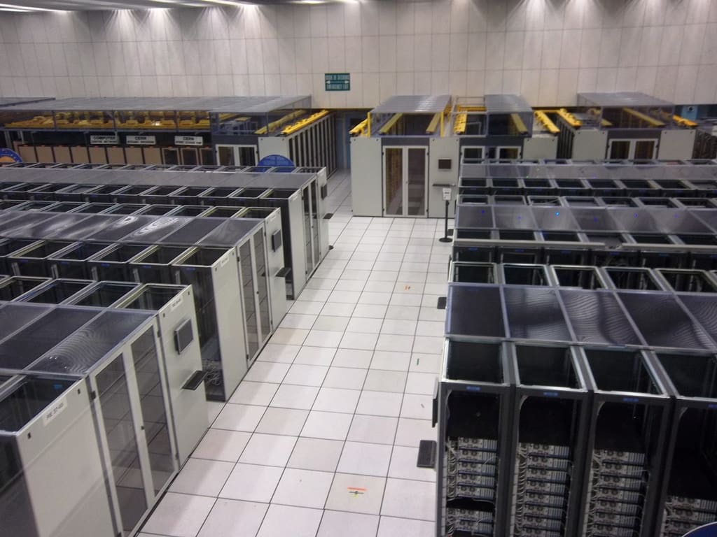 Sala de cómputo del CERN vista en altura, con múltiples pasillos de racks confinados y suelo técnico