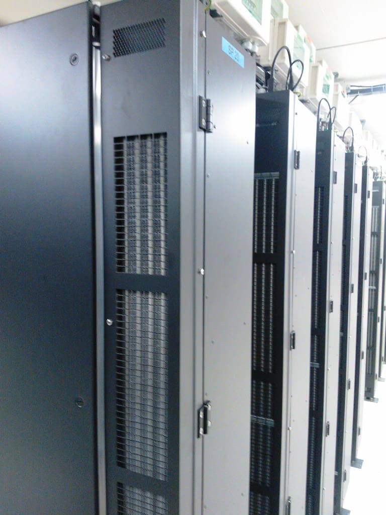 Primer plano de armarios gris oscuro con puertas de malla perforada y cables en bucle sobre la cima, etiqueta SP 20.