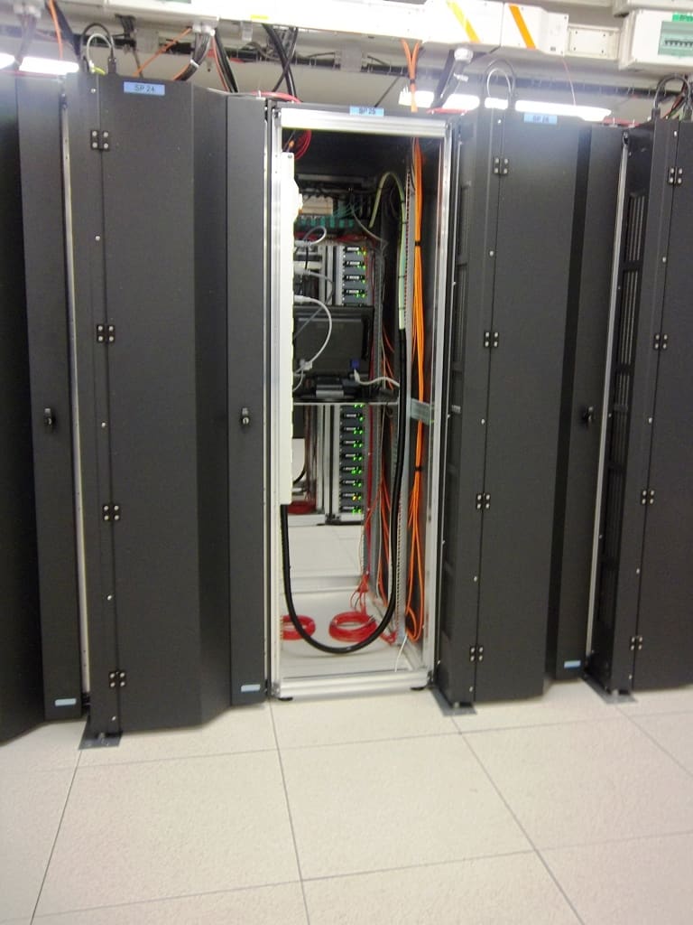 Fila de armarios negros con uno abierto que deja ver cableado interno naranja y rojo y switches de red con puertos verdes.