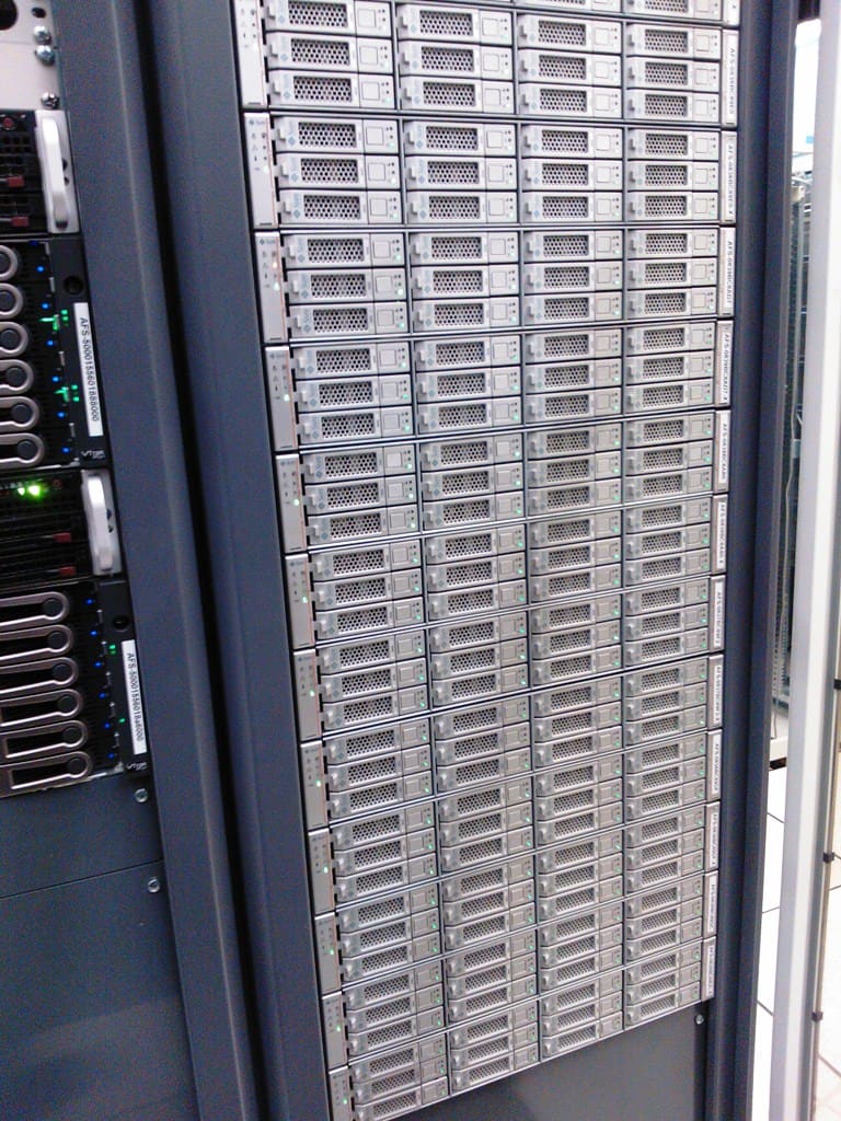 Rack repleto de servidores 1U plateados en columnas; a la izquierda módulos etiquetados con LED de estado verdes y azules.