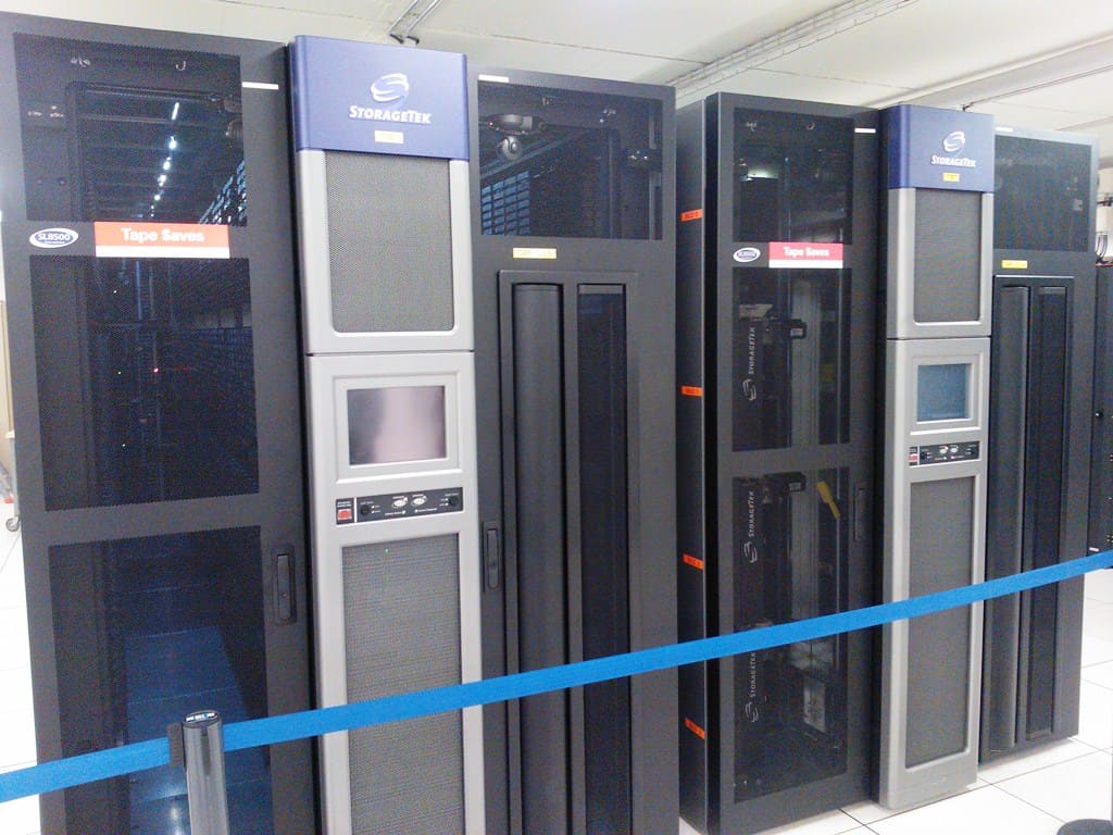 Cabinas de cintas StorageTek de tapa azul con paneles táctiles, tras cinta de balizamiento en la sala fría