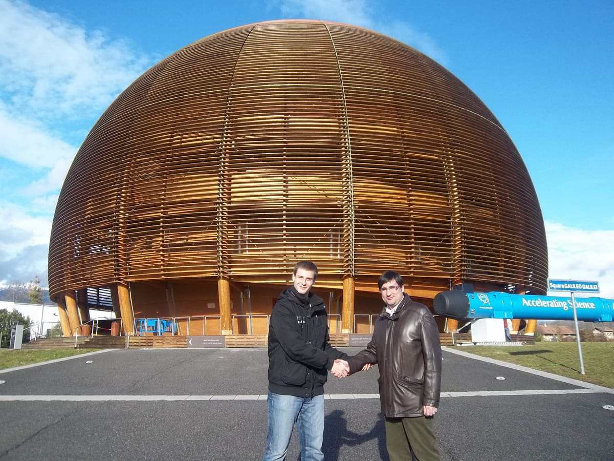Dos hombres se dan la mano ante el Globo de la Ciencia del CERN, esfera de madera bajo cielo azul