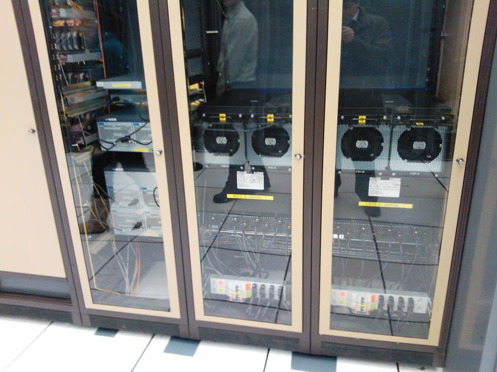 Router con módulos de ventiladores circulares tras puertas de cristal, con cableado y reflejos de personas