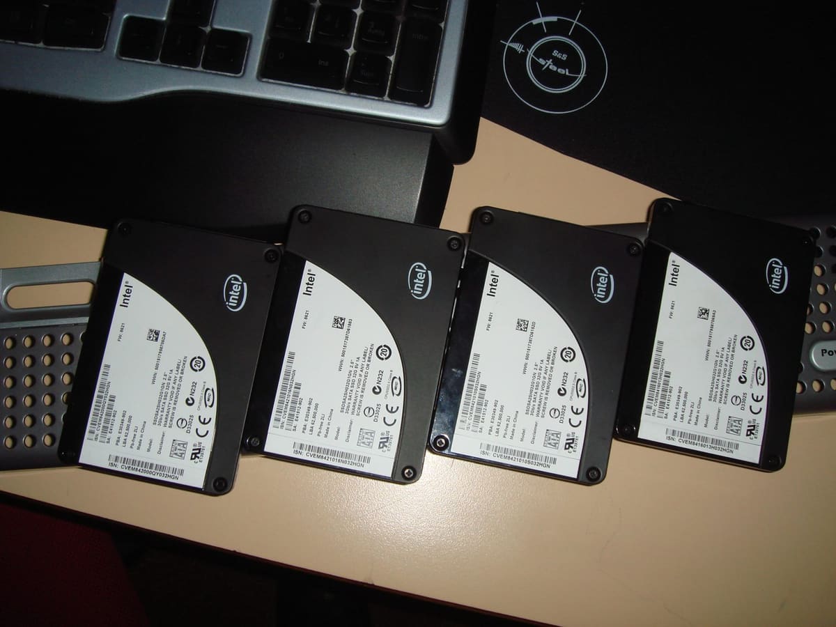 Cuatro SSD Intel de 2,5 pulgadas alineados sobre la mesa junto a un teclado y una alfombrilla.