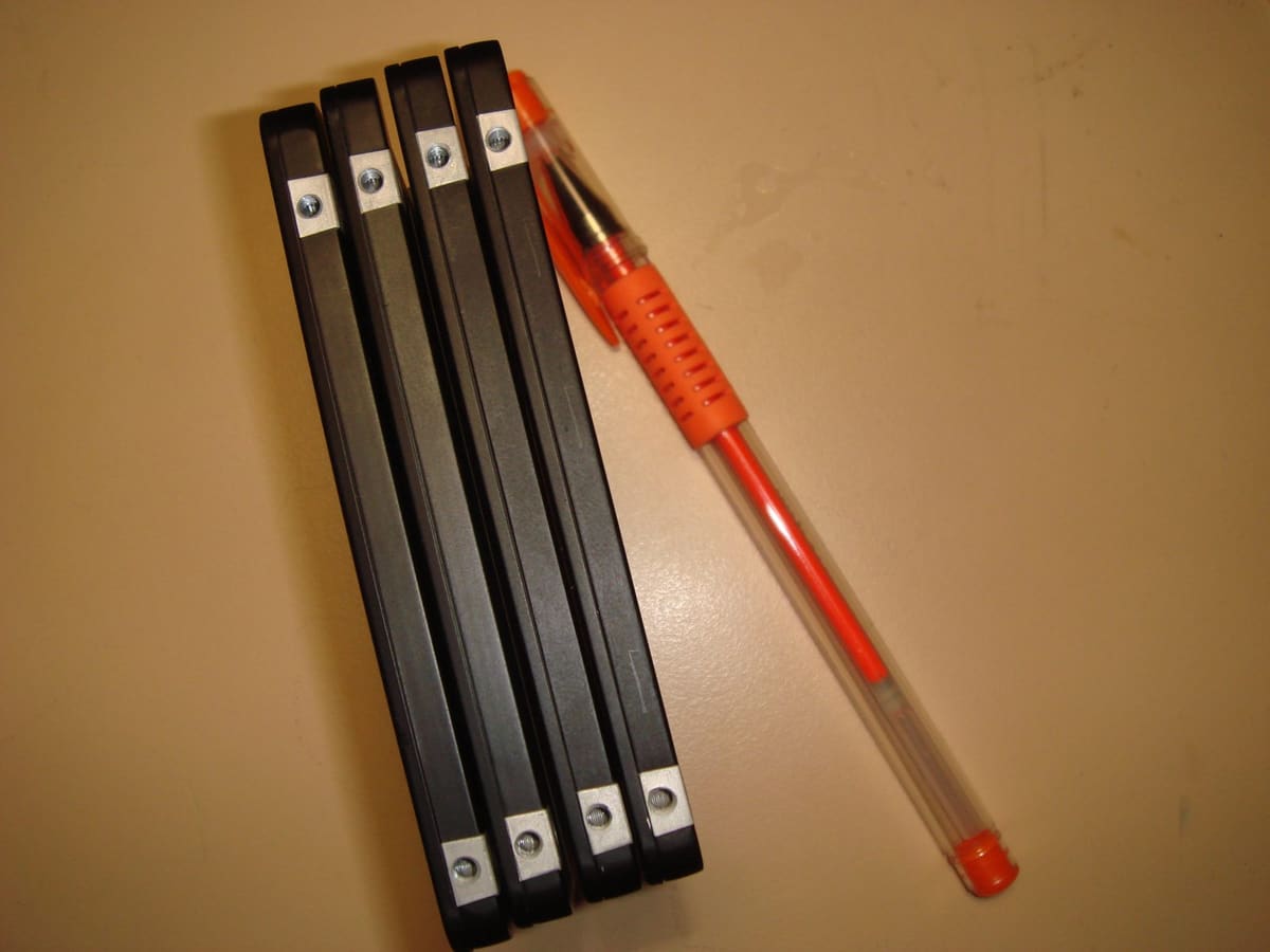 Canto de cuatro SSD apilados con tornillos de fijación, junto a un bolígrafo naranja como referencia de tamaño.