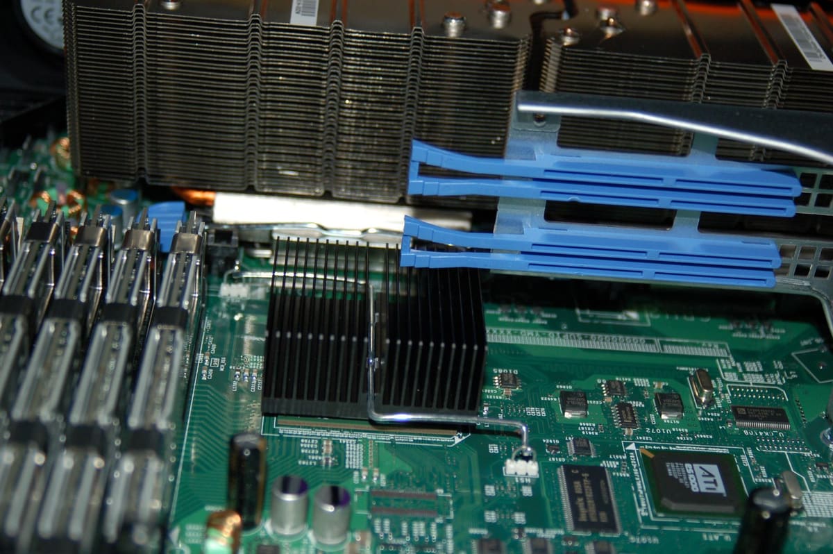 Interior de servidor: disipador de CPU con aletas, guias de aire azules y zocalos DIMM sobre placa base verde