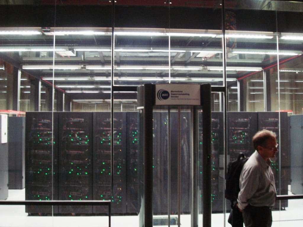 Visitante frente a la urna de cristal del MareNostrum con racks de LEDs verdes y rótulo del Barcelona Supercomputing Center