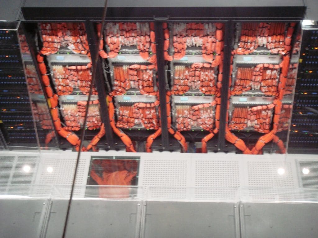 Parte trasera de armarios del supercomputador con densos mazos de cables naranjas organizados en paneles